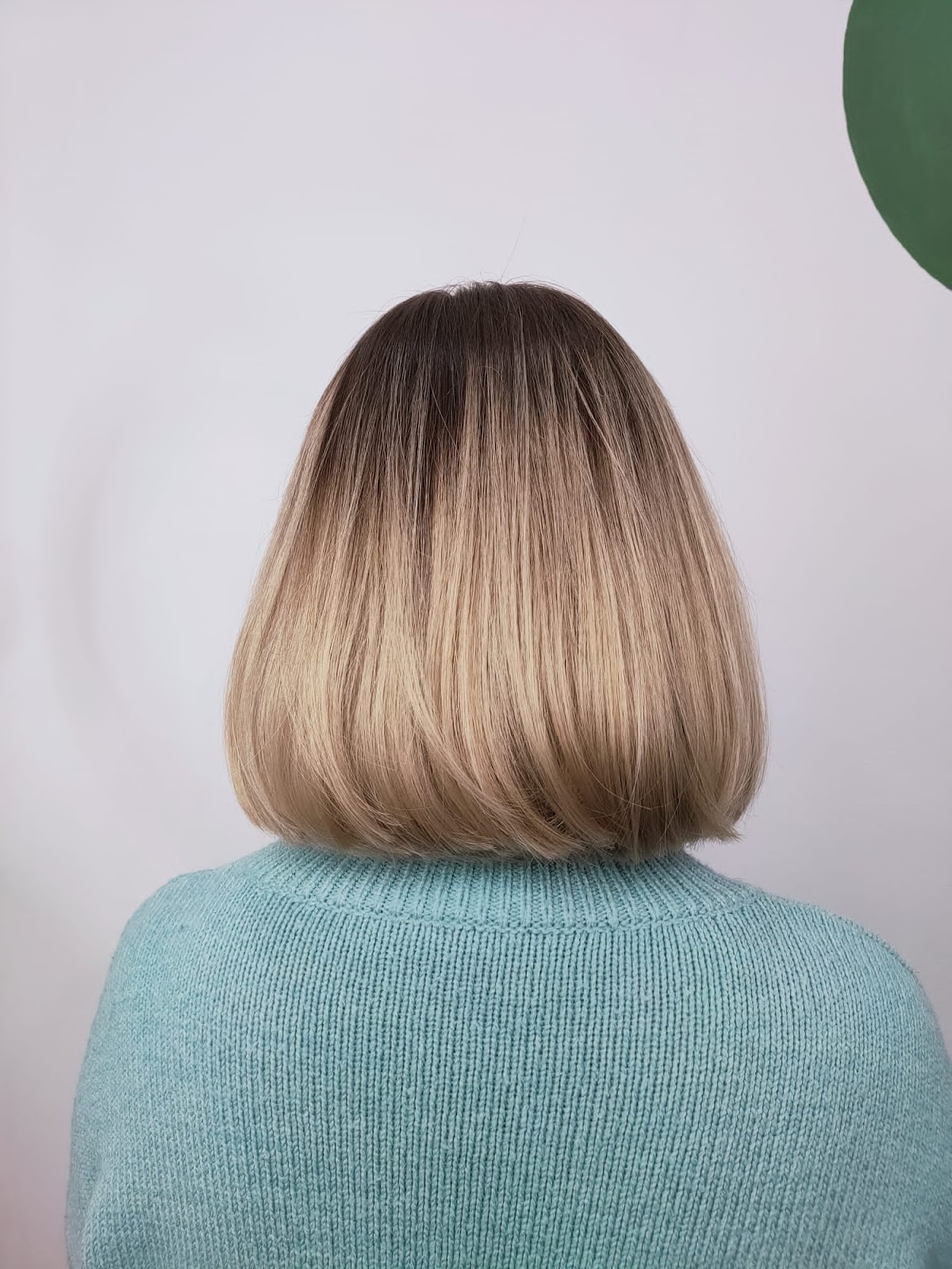 Klasyczny bob z naturalnym blond ombre, fotografowany przy zielonej ścianie